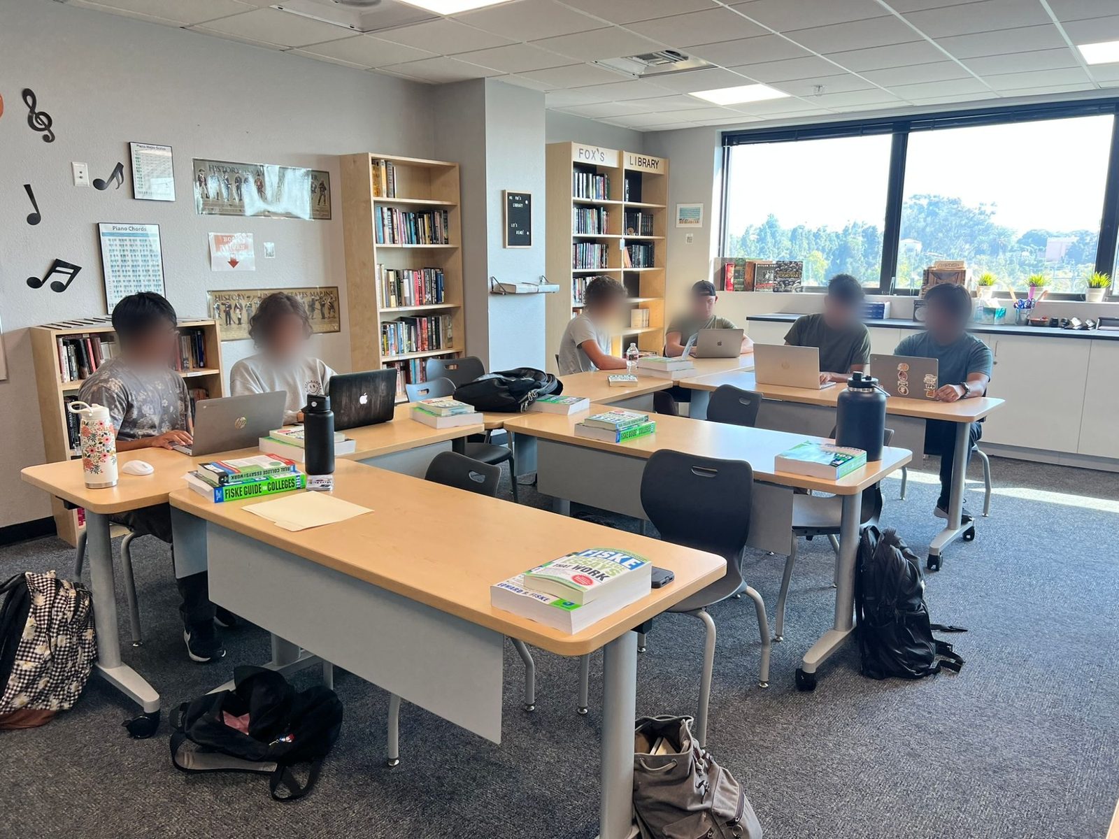 Students researching colleges on laptops with Fiske college guides in Taylor Fox's classroom library