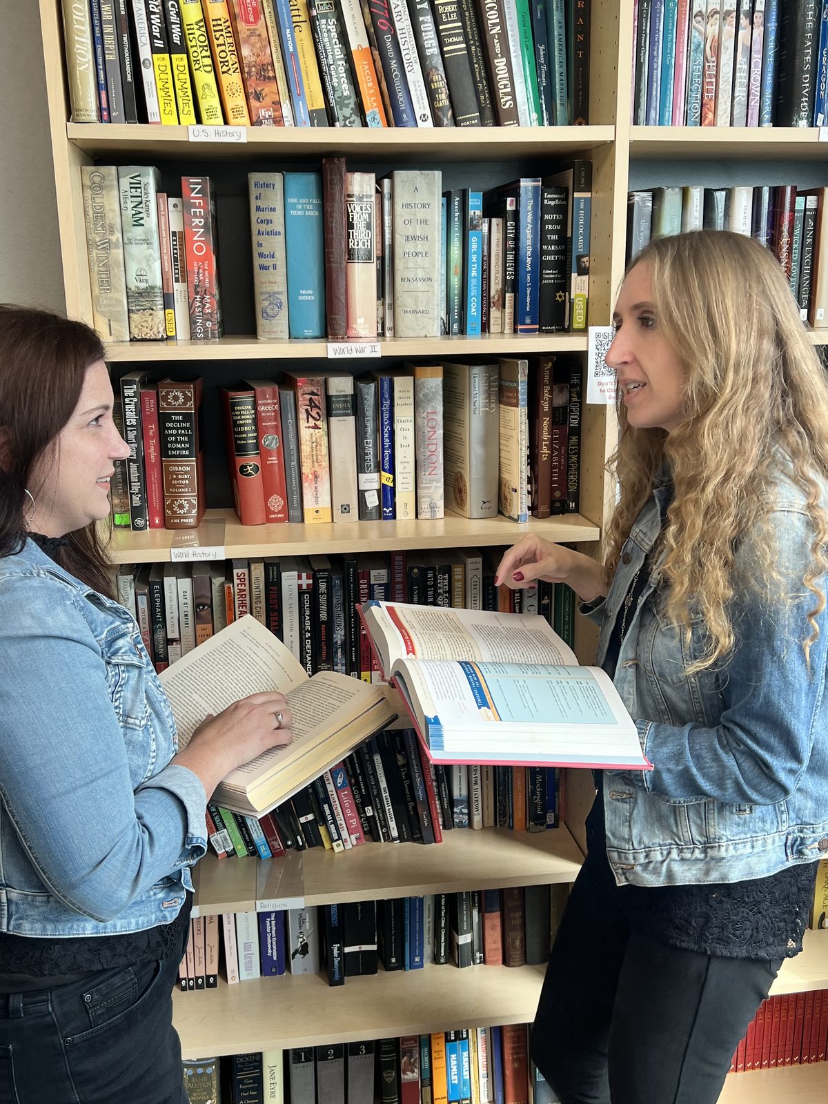 Taylor Fox and a colleague talking through two open history books in front of a classroom library
